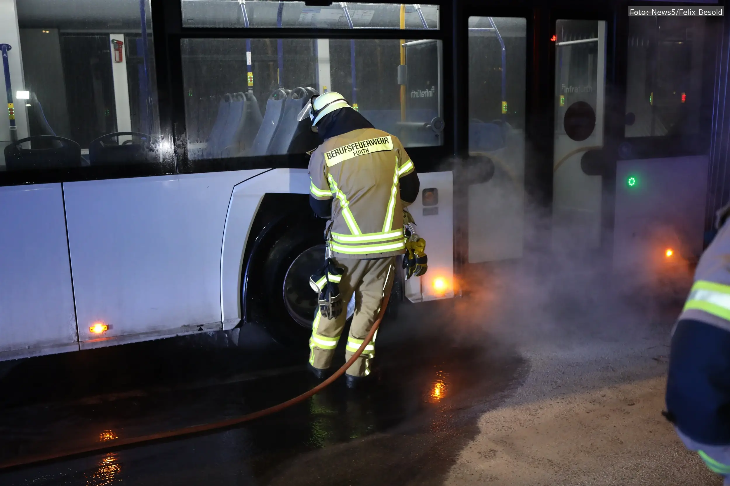 Ein Feuerwehrmann löscht die Flammen an einem Linienbus in Fürth.